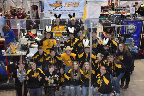 The robotics team is shown in front of their pit wearing black bunny ears.