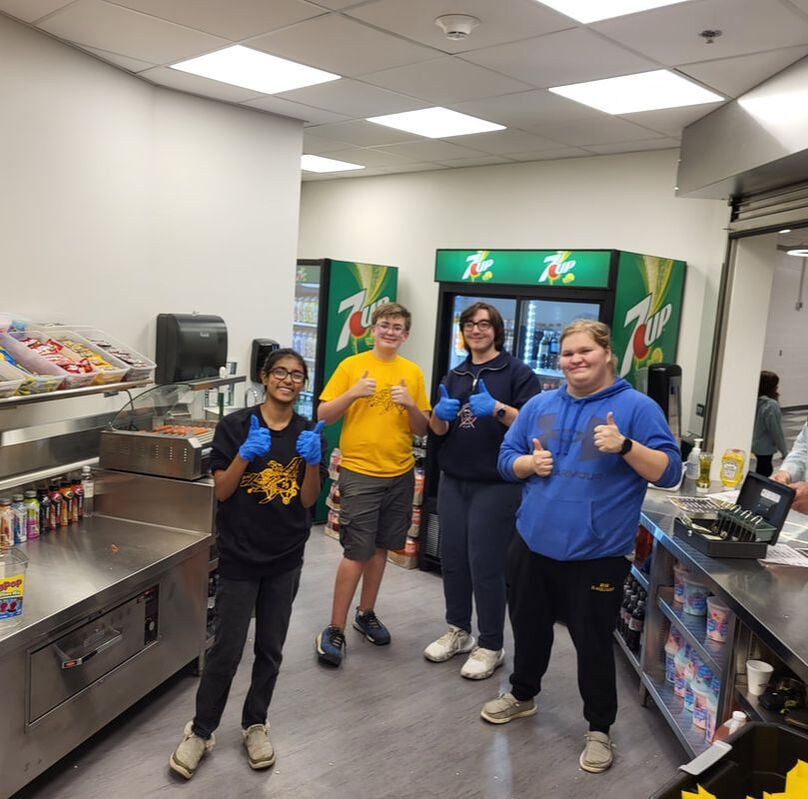Four robotics team members stand in the concession stand giving the camera a 